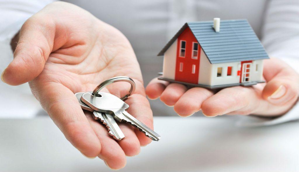 Persona sosteniendo con la mano izquierda una casa, mientras en la mano derecha sostiene unas llaves de una vivienda