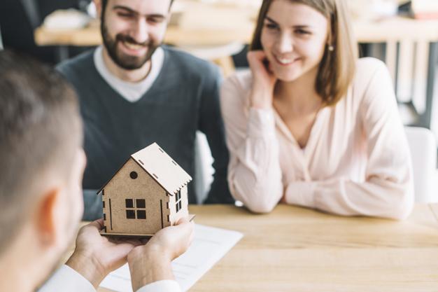 Representante inmobiliario sosteniendo casa en forma de maqueta mientras una pareja está feliz