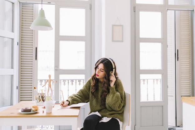 Chica con unos cascos escuchando música mientras escribe en un papel