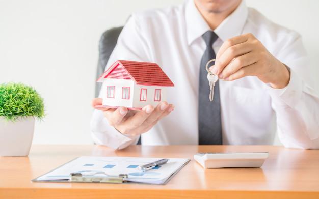 Representante inmobiliario sosteniendo una casa en forma de maqueta y unas llaves mientras realiza la tasación de una casa