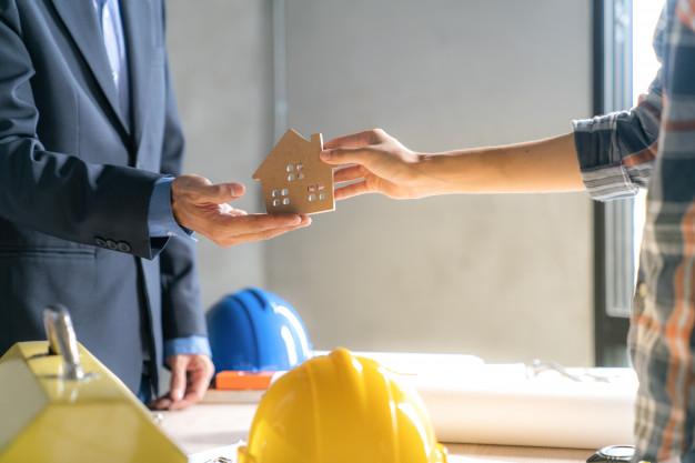Representante inmobiliario y cliente sosteniendo una casa en forma de maqueta