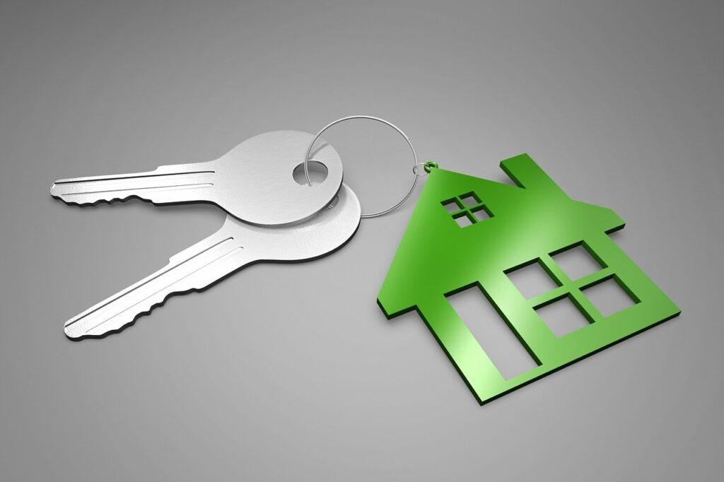 Llaves de una casa mientras al lado hay una casa de color verde en forma de llavero